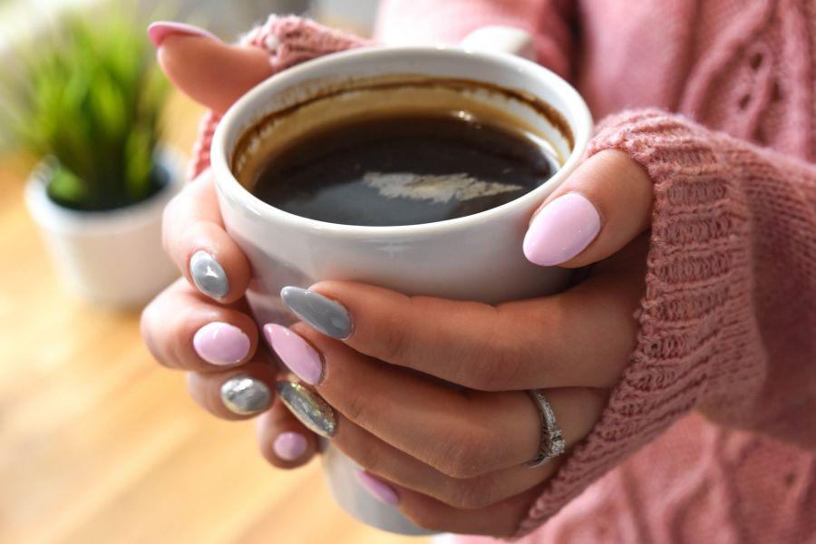taza llena de café sostenida por unas manos de mujer con las uñas pintadas